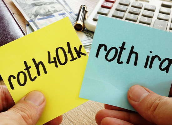 Two hands holding sticky notes, one yellow with 'roth 401k' written on it and one blue with 'roth ira' written on it, over a desk with money, a pen, and a calculator.