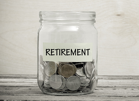 A glass jar labeled 'RETIREMENT' containing a small amount of coins sits on a wooden surface, symbolizing the concept of saving money for retirement.
