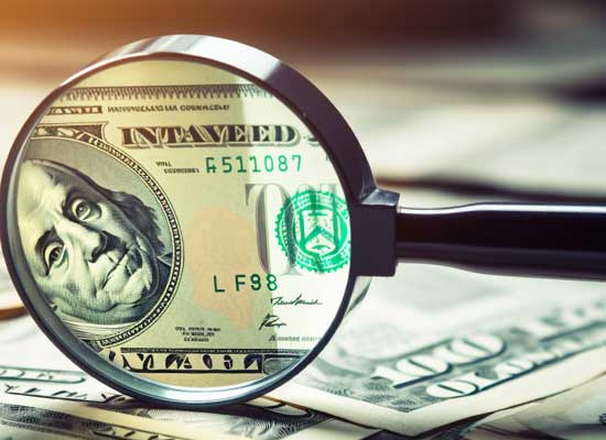 A magnifying glass focusing on a hundred-dollar bill, highlighting the importance of careful retirement income planning.