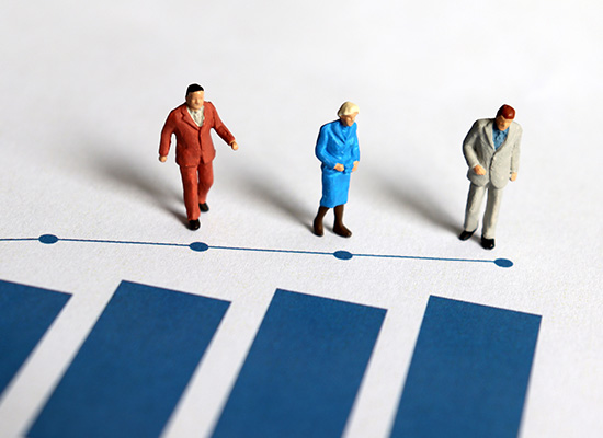 Miniature figurines of three people, each dressed differently, walking along a line graph, depicting the progression of retirement ages or financial states.