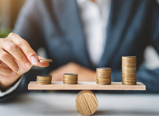 A person balances stacks of coins on a wooden scale, illustrating the careful management of retirement income and personal finance.