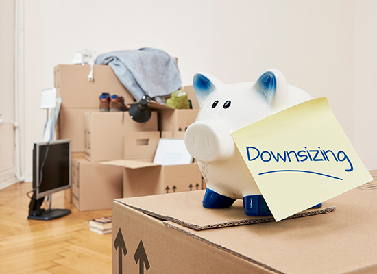 A piggy bank labeled "Downsizing" sits on a moving box, symbolizing the trend of retirees reducing living costs to manage retirement expectations.