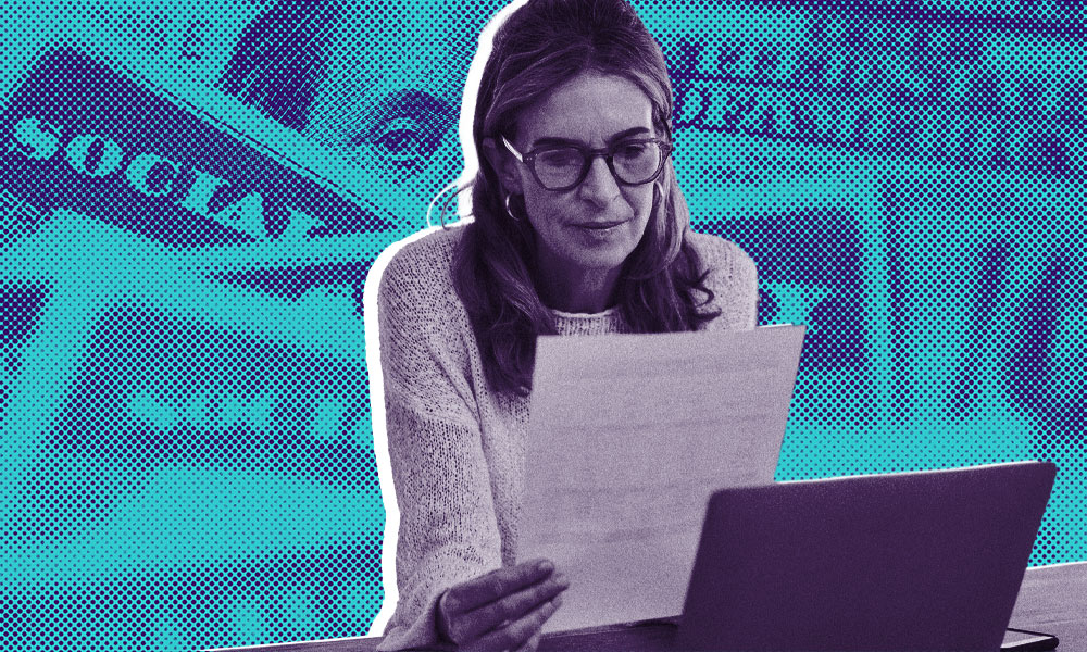 A woman wearing glasses is reading a piece of paper in front of a laptop.