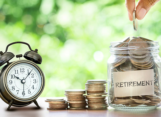 An alarm clock sits beside stacks of coins, symbolizing the ticking countdown to your financial future. A hand drops a coin into a jar labeled 'RETIREMENT', filled with coins