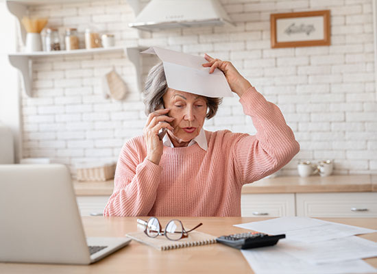 An older woman in a pink sweater sits at a kitchen table, discussing her annuity on the phone