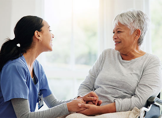A caregiver in a blue uniform and an elderly woman with short gray hair are smiling at each other, their connection evident as they discuss retirement income strategies