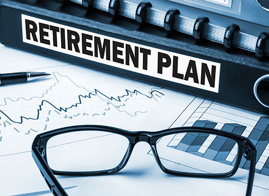 A close-up image of a binder labeled 'Retirement Plan' on a desk. In front of it are glasses, a pen, financial charts, and graphs.