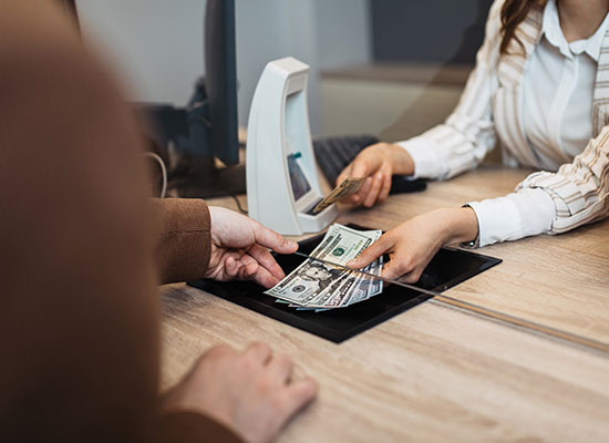 A bank teller hands cash to a customer, symbolizing retirement withdrawals, retirement distribution methods, and systematic withdrawals.