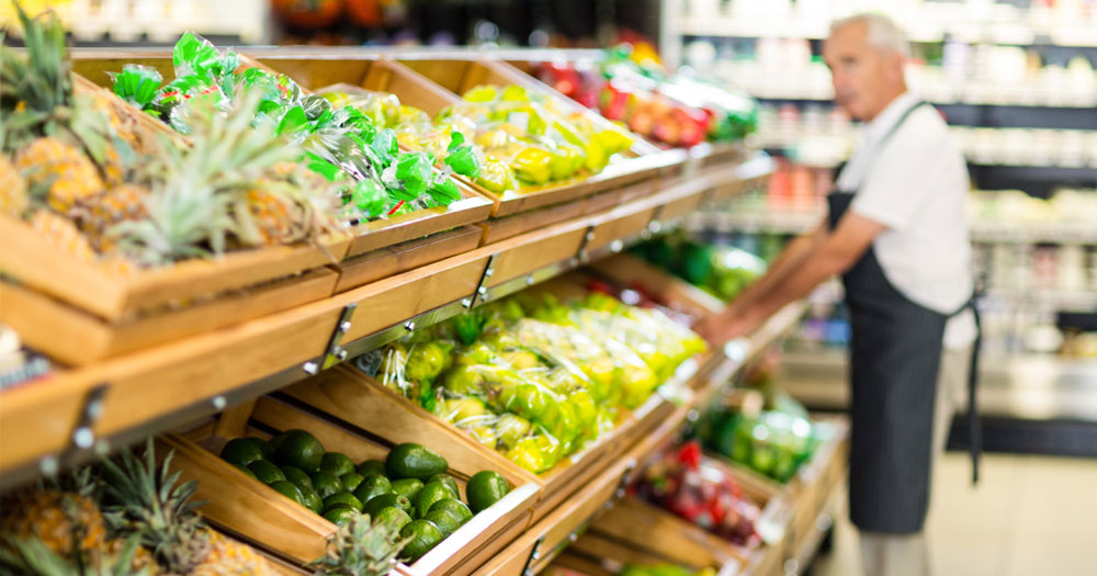 Fruit and vegetable aisle in the grocery store with an elderly man stocking the shelves