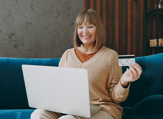 A woman looking happy while looking at her laptop and holding a credit card.