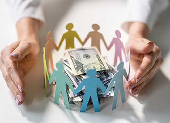 Hands protectively encircle paper cutouts of people surrounding stacks of money, representing the concept of safeguarding family wealth and the importance of financial planning for future generations.