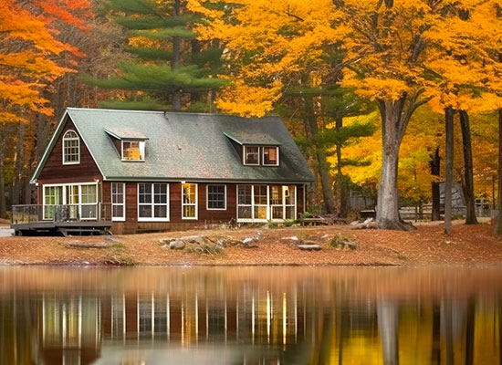 A cozy brown vacation home with a green roof sits surrounded by vibrant autumn foliage.