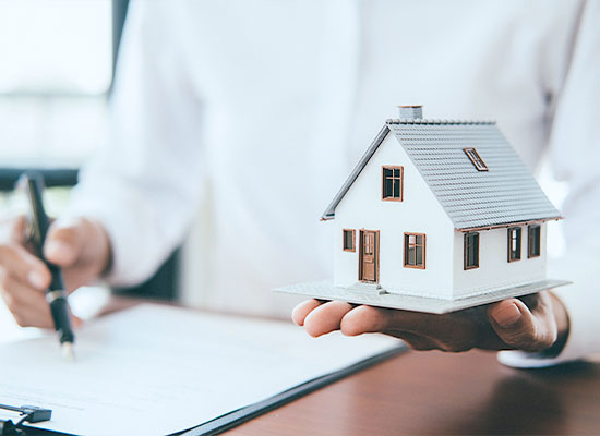 A person holds a small model of a vacation home in one hand while signing a document with the other hand.