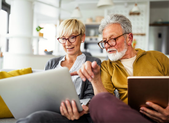 A couple reviews retirement and estate planning options on their computer in their home, considering Medicaid eligibility and income and asset limits to protect their estate from estate recovery