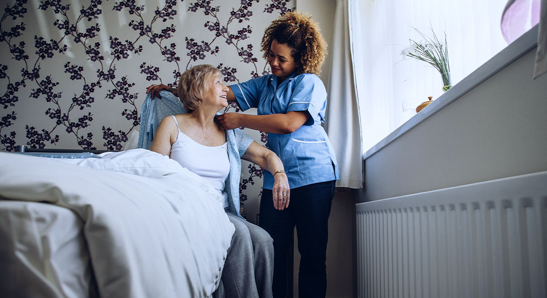 A photo of a caregiver helping a lady by helping her put on her shirt