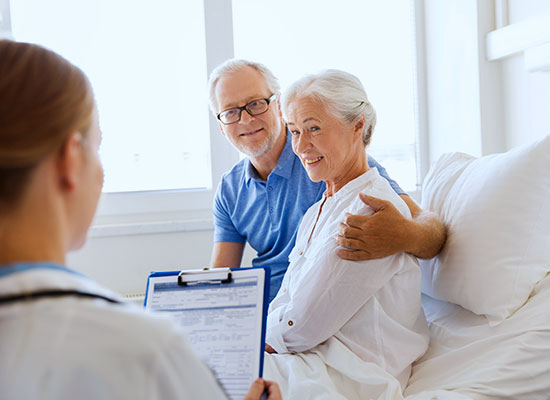 A photo of a smiling man and a woman listening to a caregiver holding a clipboard