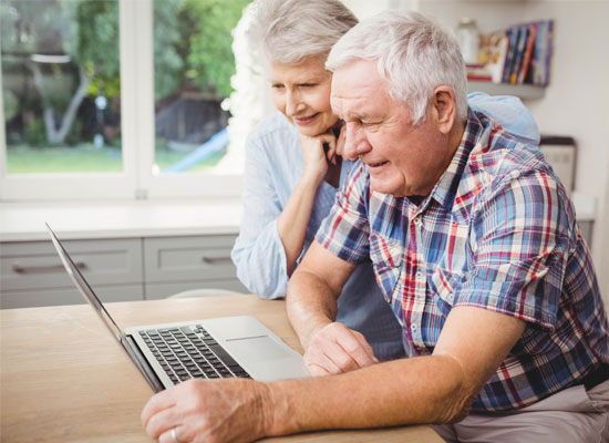 A senior couple reviews long-term care policies and Medicaid benefits on their laptop, planning for retirement and elder care with their family.
