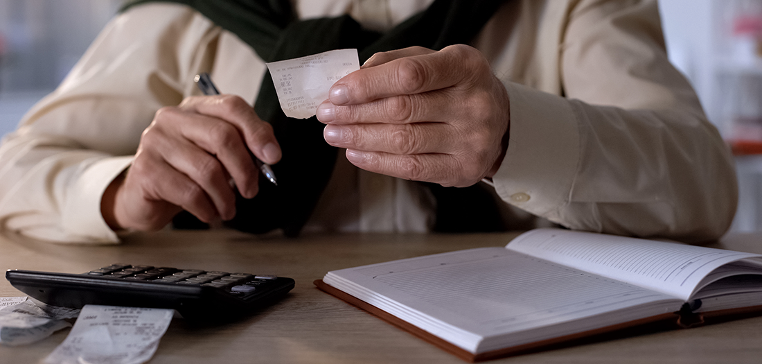 Sitting in front of a calculator and planning book, old man goes over his expenses