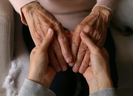 A close-up of an elderly person’s wrinkled hands being held by a younger individual, symbolizing the emotional connection and responsibility of unpaid care for aging parents.