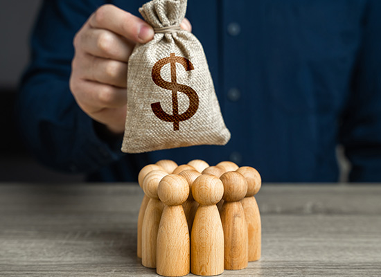 A person holding a bag with a dollar sign above a group of wooden figures, representing financial distribution or planning.