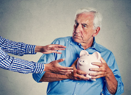 An elderly man with white hair, wearing a blue shirt, clutches a pink piggy bank tightly to his chest while looking suspiciously at two hands reaching out towards him, wary of identity theft.