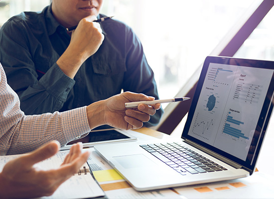 Business professionals analyze financial data and graphs on a laptop, demonstrating collaborative financial descision-making.