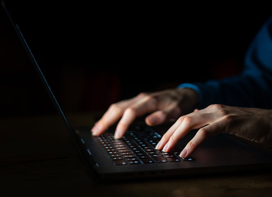 Close-up of a person typing on a laptop keyboard with a dark background
