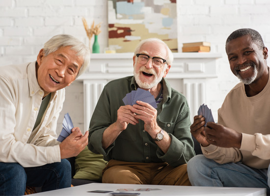 Three older men, representing diverse older Americans, enjoy a card game, highlighting community connections and support networks for aging in place.