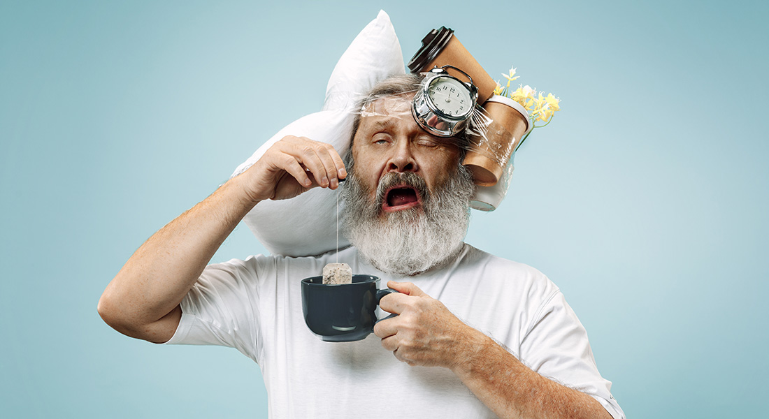 Overworked and tired old man yawns with items taped to his head and teacup in hand