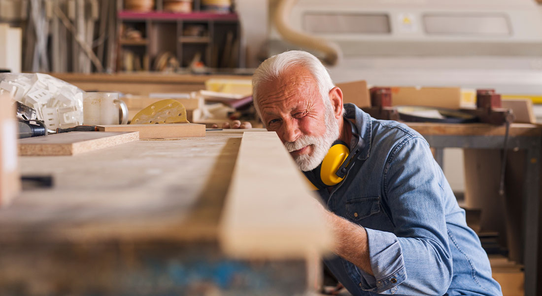 an older man working by cutting a piece of wood