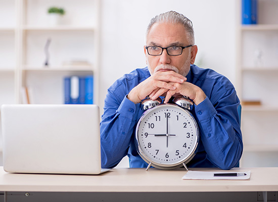 older man leaning against a clock looking at his laptop