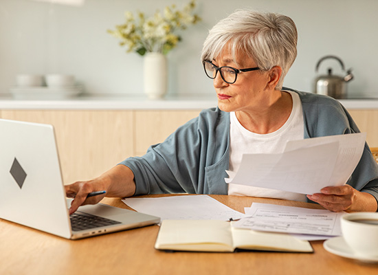 An elderly woman reviews documents on her laptop, representing flexible retirement options and planning.