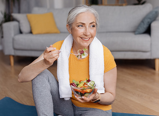 A woman enjoying a healthy salad post-workout, representing lifestyle changes and health care priorities during retirement.