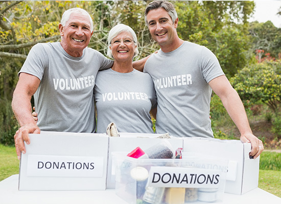 Three volunteers smile while organizing donations, highlighting the importance of community involvement and social connections for solo agers in retirement.