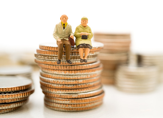 Miniature elderly couple figurines sit atop stacks of coins, representing retirement savings and financial planning for seniors.