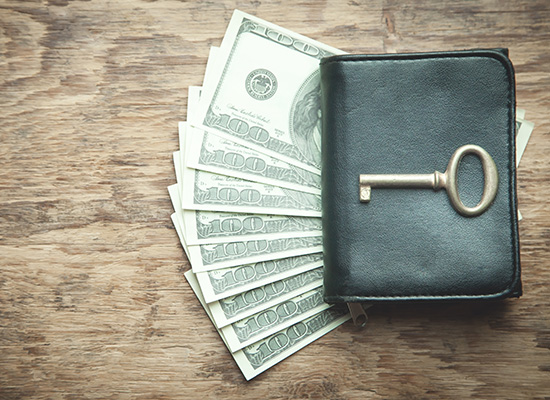 A black wallet with a key placed on top, surrounded by fanned-out cash