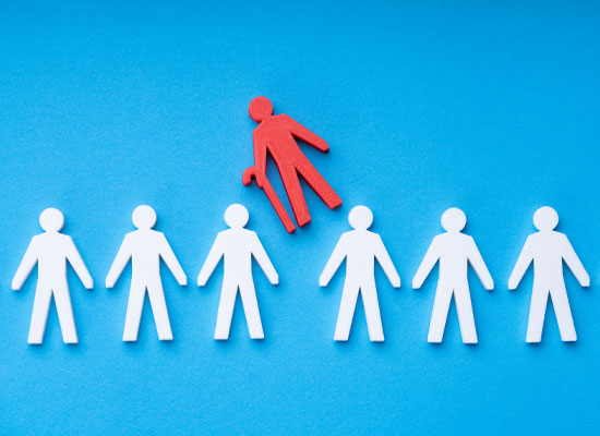 A red cutout figure of an older American with a cane stands apart from a line of white figures, symbolizing potential age discrimination against seniors and older workers in employment and their careers before retirement.