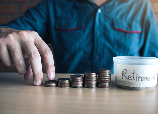A person stacks coins in ascending order next to a container labeled 'Retirement,' symbolizing retirement savings and financial planning for the future.