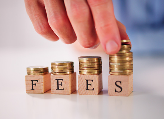 A hand stacking coins on blocks spelling 'FEES', indicating the financial costs or fees associated with transactions or services.