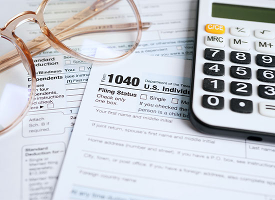 A close-up view of a U.S. tax form 1040 with a calculator, eyeglasses, and other tax documents related to retirement scattered around it.