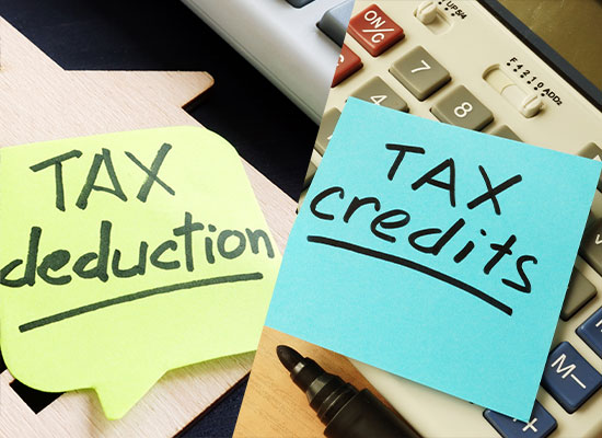 Sticky notes reading 'TAX deduction' on yellow and 'TAX credits' on blue lie atop calculators