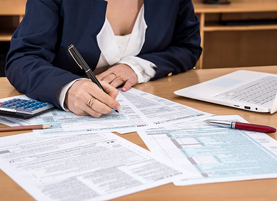 A person in a suit diligently fills out paperwork on a desk equipped with a laptop, calculator, and pen—engaging in meticulous tax preparation.