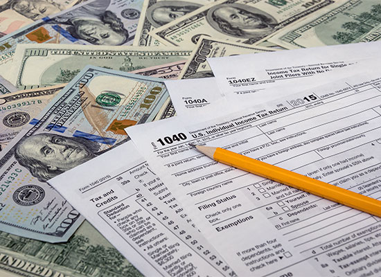 A pile of U.S. dollar bills in various denominations surrounds completed tax forms, including a 1040 form